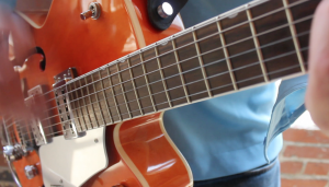 Close-up view of a person from a Boston wedding band playing an orange electric guitar, focusing on the fretboard and strings, with a partial view of their blue shirt.